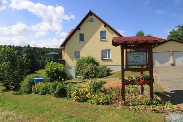 Yellow house in flower garden in front of forest scenery